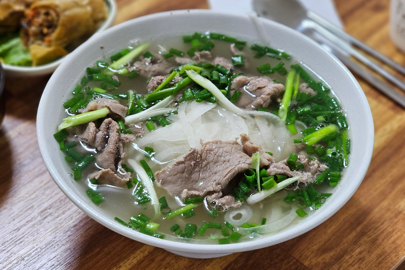 A bowl of traditional Vietnamese beef pho served with fresh herbs, rice noodles, and clear broth.