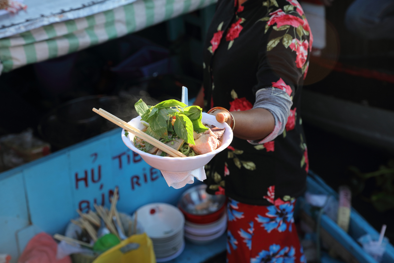 boat at Cai Rang Floating Market, one of the Mekong Delta's most authentic culinary experiences.A local vendor serves a bowl of traditional Vietnamese noodles from a boat at Cai Rang Floating Market