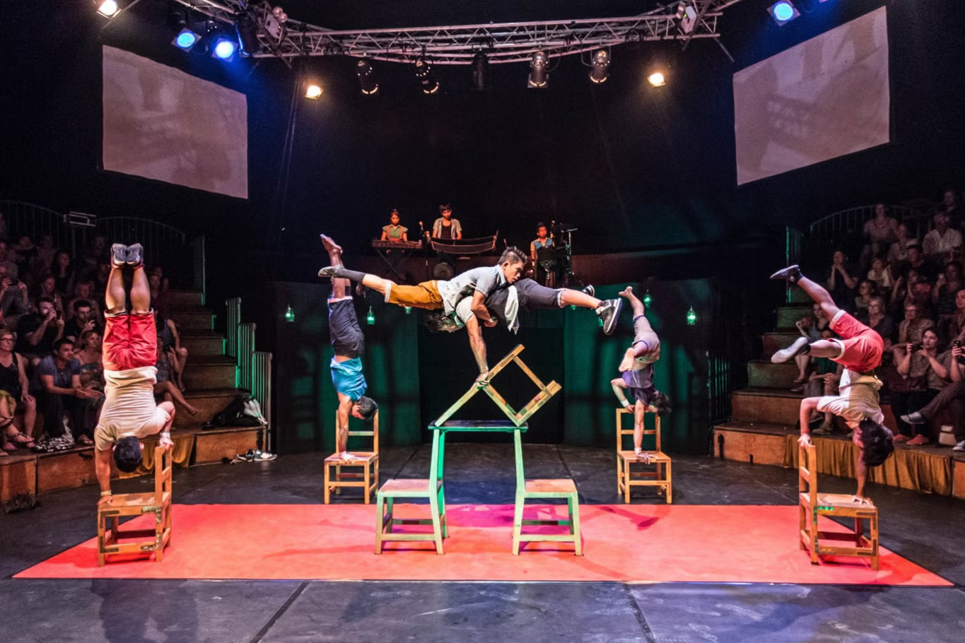 Cambodian acrobats dynamic balancing performance on stacked wooden chairs in circus setting.