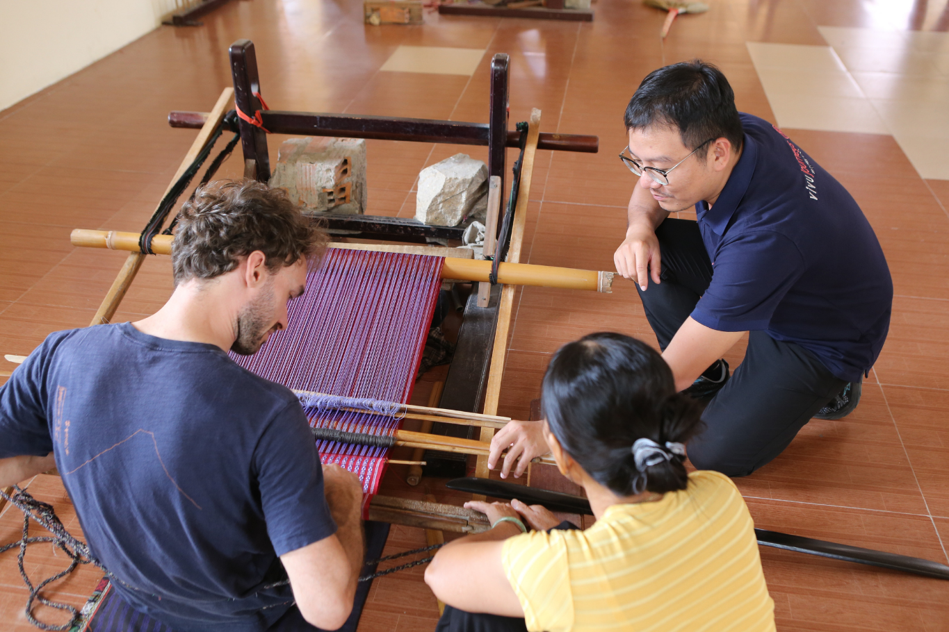 Local Vietnamese elder artisan smiling at weaving wheel for first-time travelers