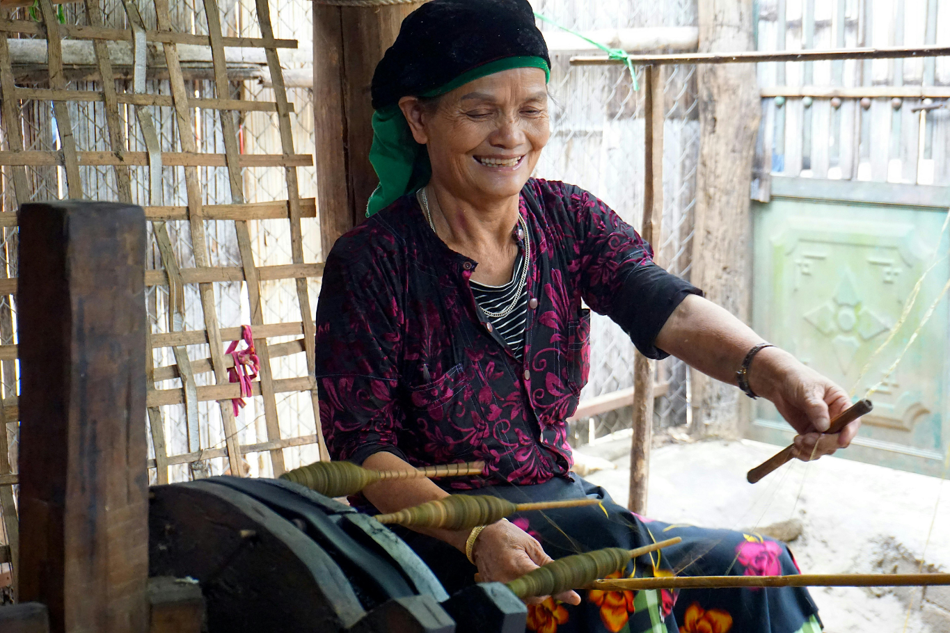 Smiling local artisan weaving thread on a traditional spinning wheel in Vietnam