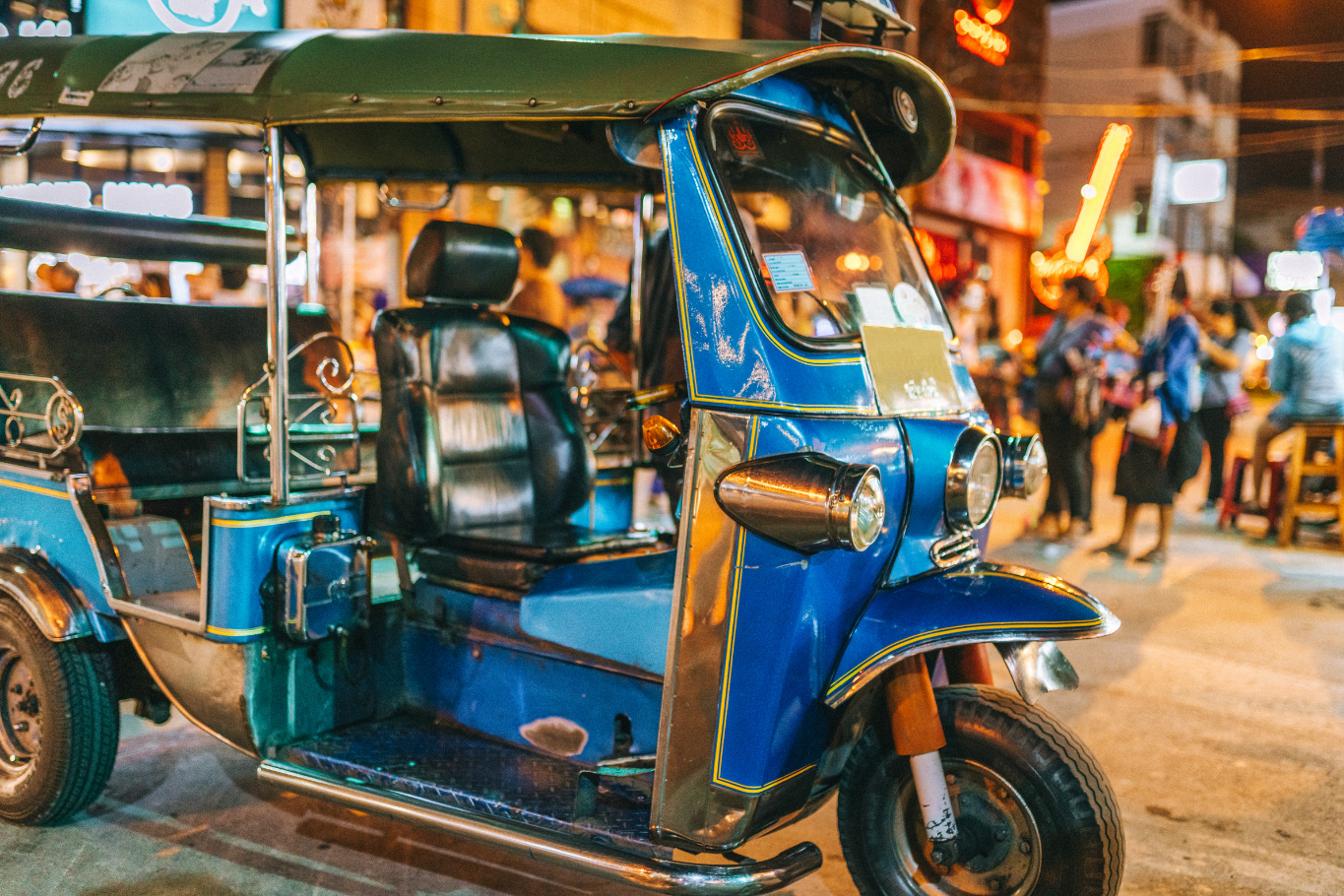 A vibrant tuk-tuk parked on a busy, illuminated street in Thailand