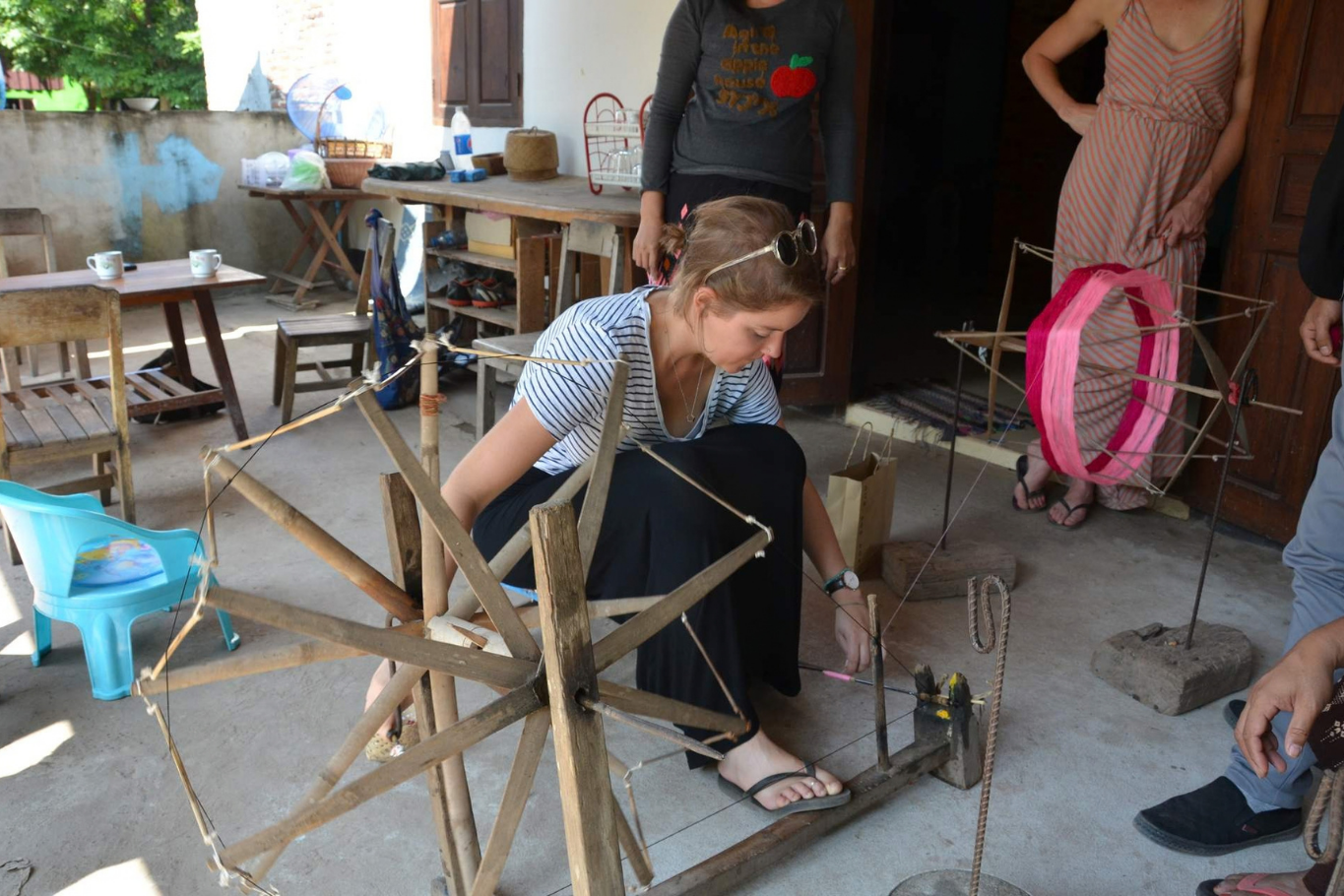 A female traveler sitting and learning how to use a traditional wooden spinning wheel.